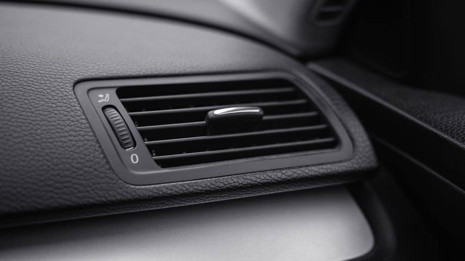 a close up of a air vent in a car.|two hands are holding a couple of wires.|a person holding a blow dryer on a sidewalk.|a man is working on a car's steering wheel.