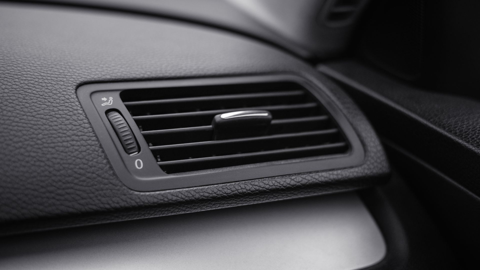 a close up of a air vent in a car.|two hands are holding a couple of wires.|a person holding a blow dryer on a sidewalk.|a man is working on a car's steering wheel.
