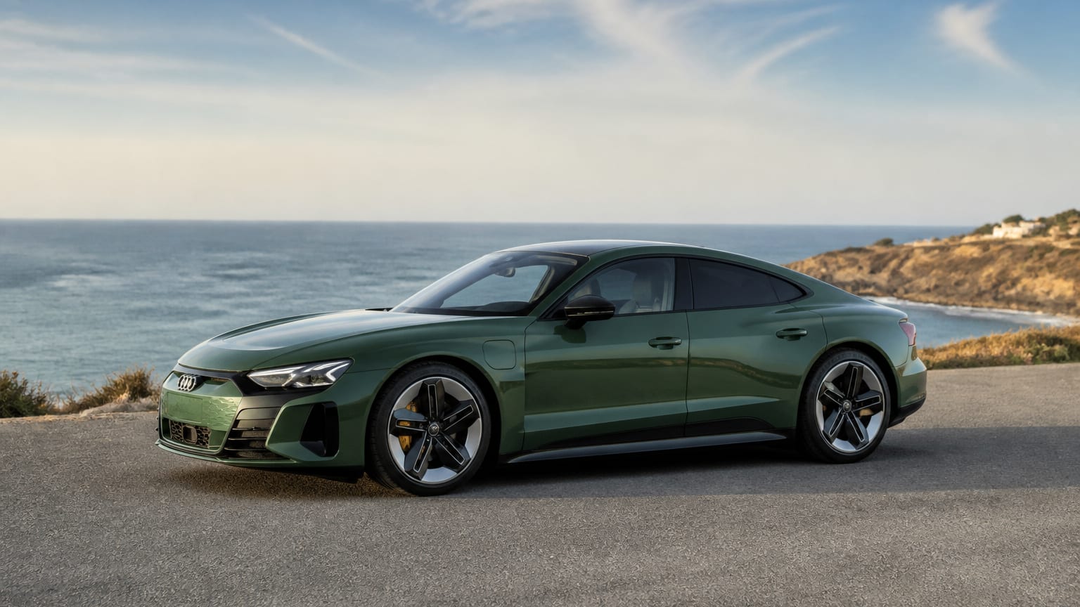A green Audi e-tron GT electric sport sedan parked on a coastal overlook.