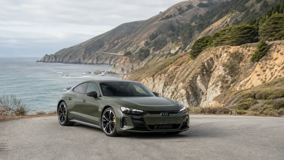 A Tactical Green Audi e-tron GT electric sport sedan, three-quarter front view, parked on a coastal canyon road.