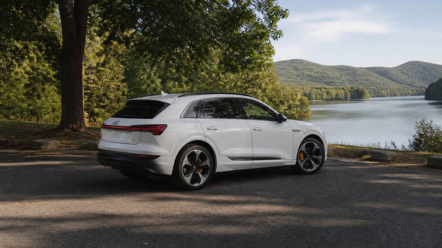 A white Audi e-tron electric SUV parked beside a modern charging station.