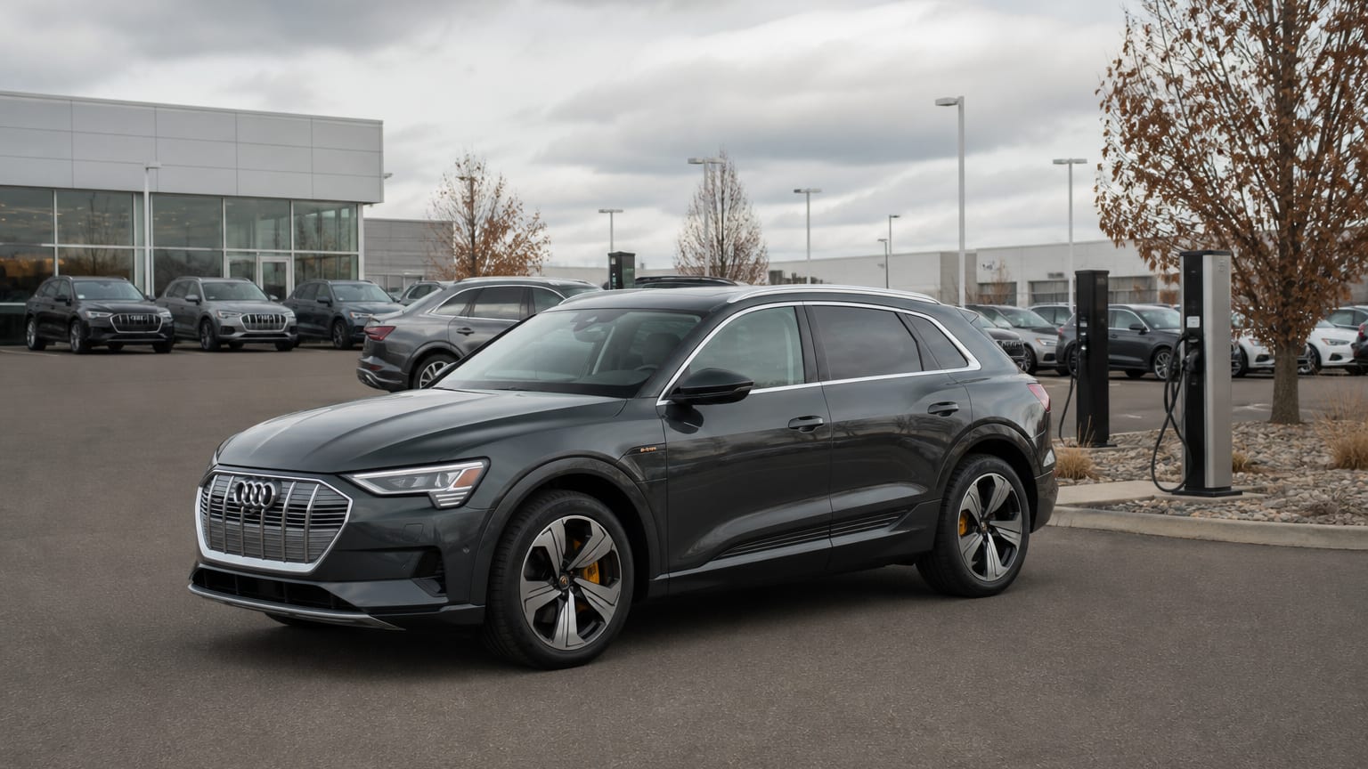 A dark gray 2019 Audi e-tron parked in a dealership lot near a charger.