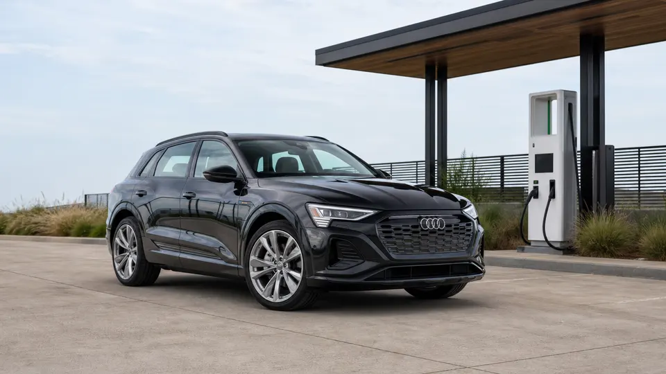 A Mythos Black Audi Q8 e-tron electric SUV, three-quarter front view, parked at a modern charging plaza.