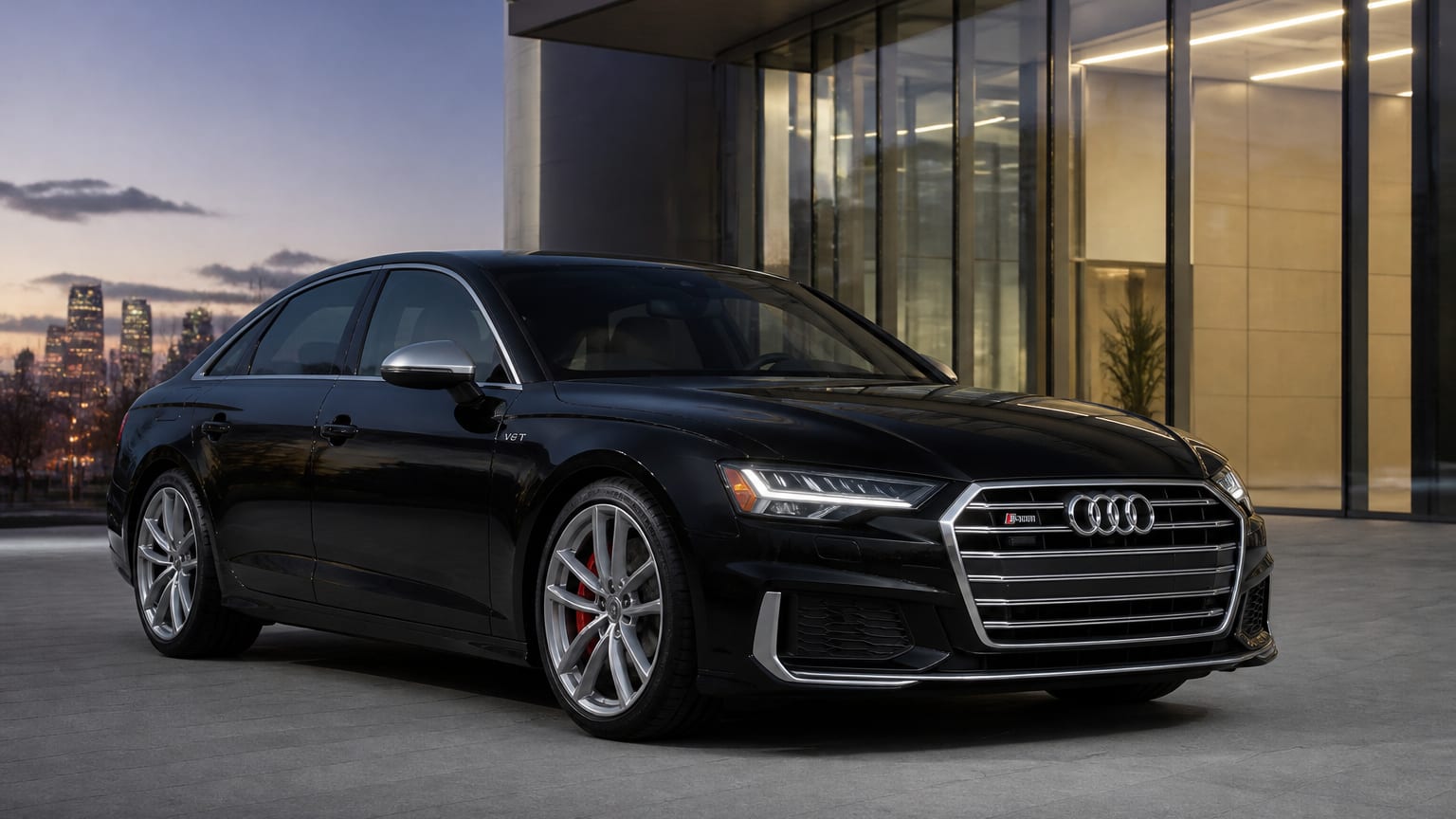 A Mythos Black Audi S6 sedan parked outside a glass office building.