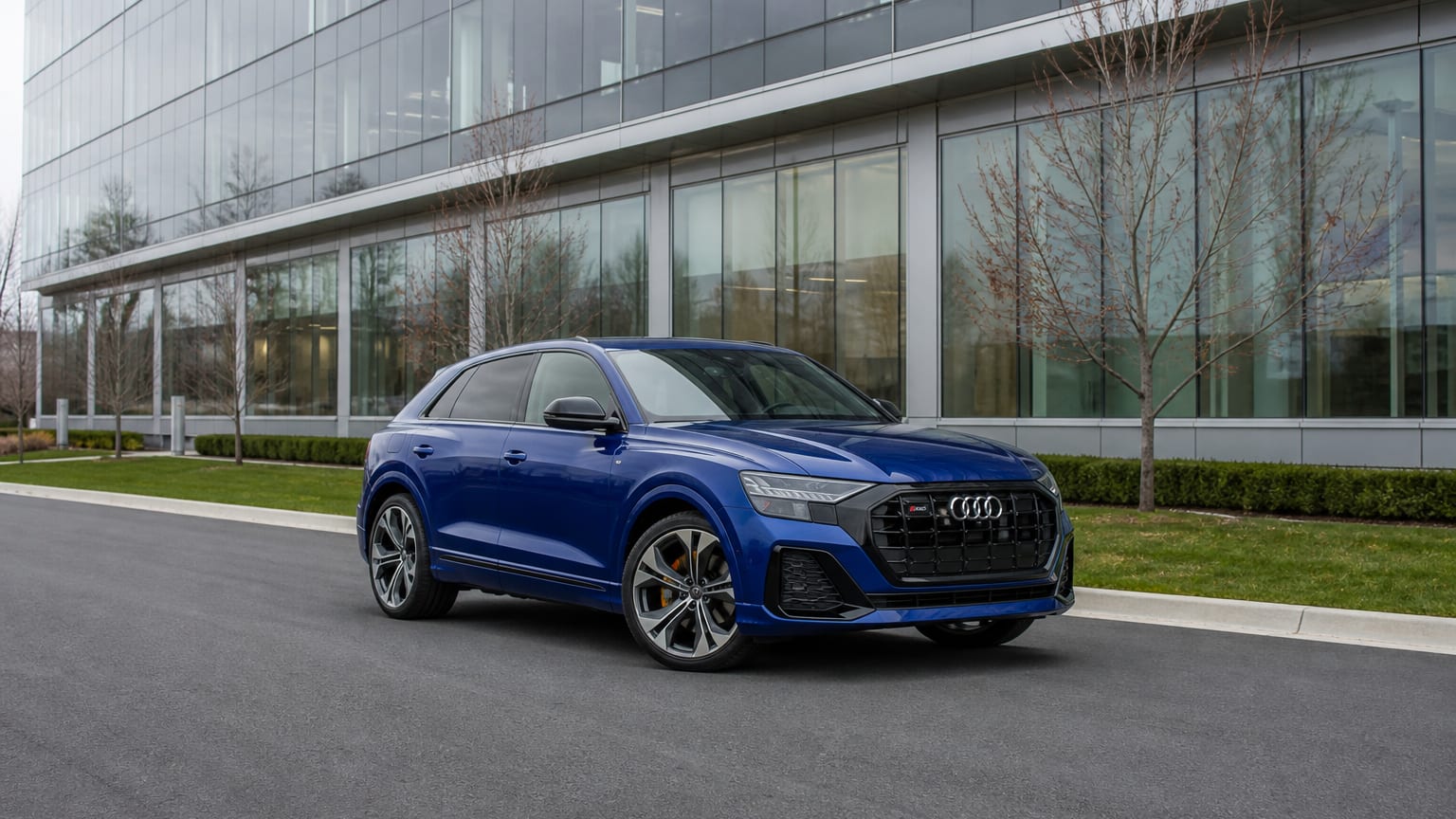 A Navarra Blue Audi SQ8 parked outside a glass office building.