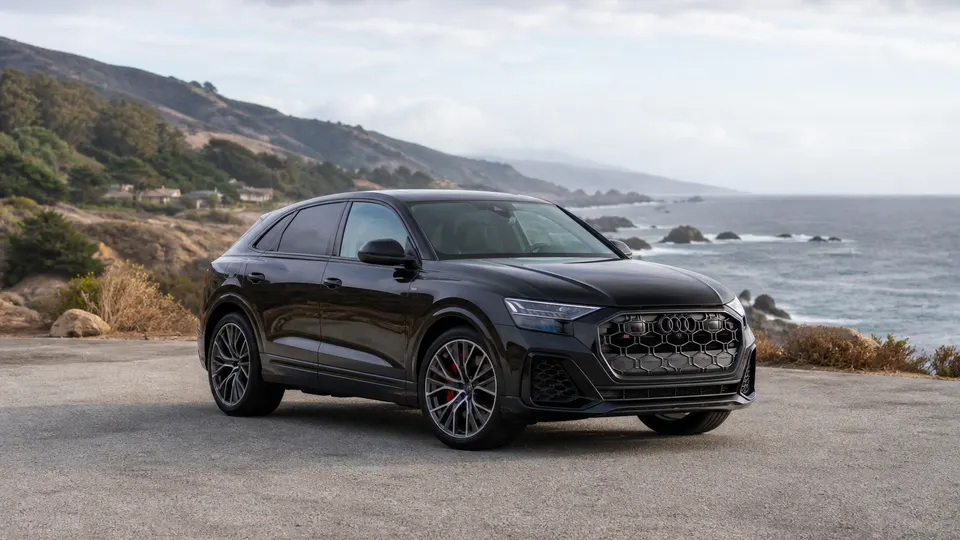 A Mythos Black Audi SQ8 performance SUV, three-quarter front view, on a coastal road.