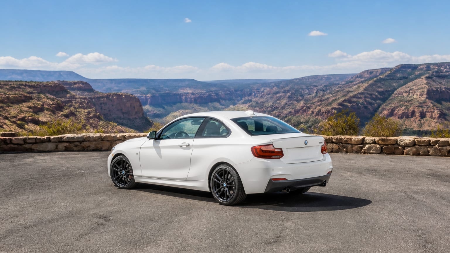 A white BMW 2 Series coupe parked on an empty canyon road overlook.