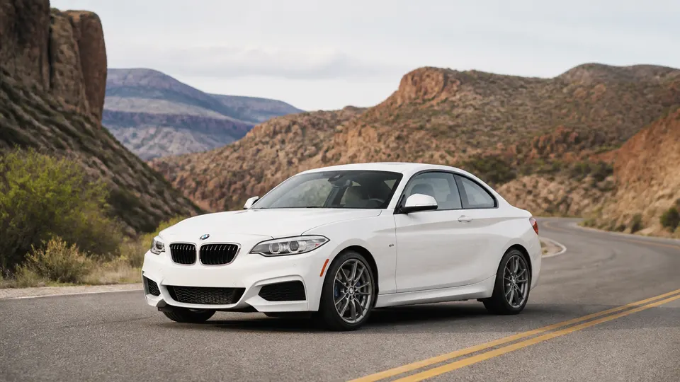 An Alpine White BMW 2 Series coupe, three-quarter front view, parked on an empty canyon road.