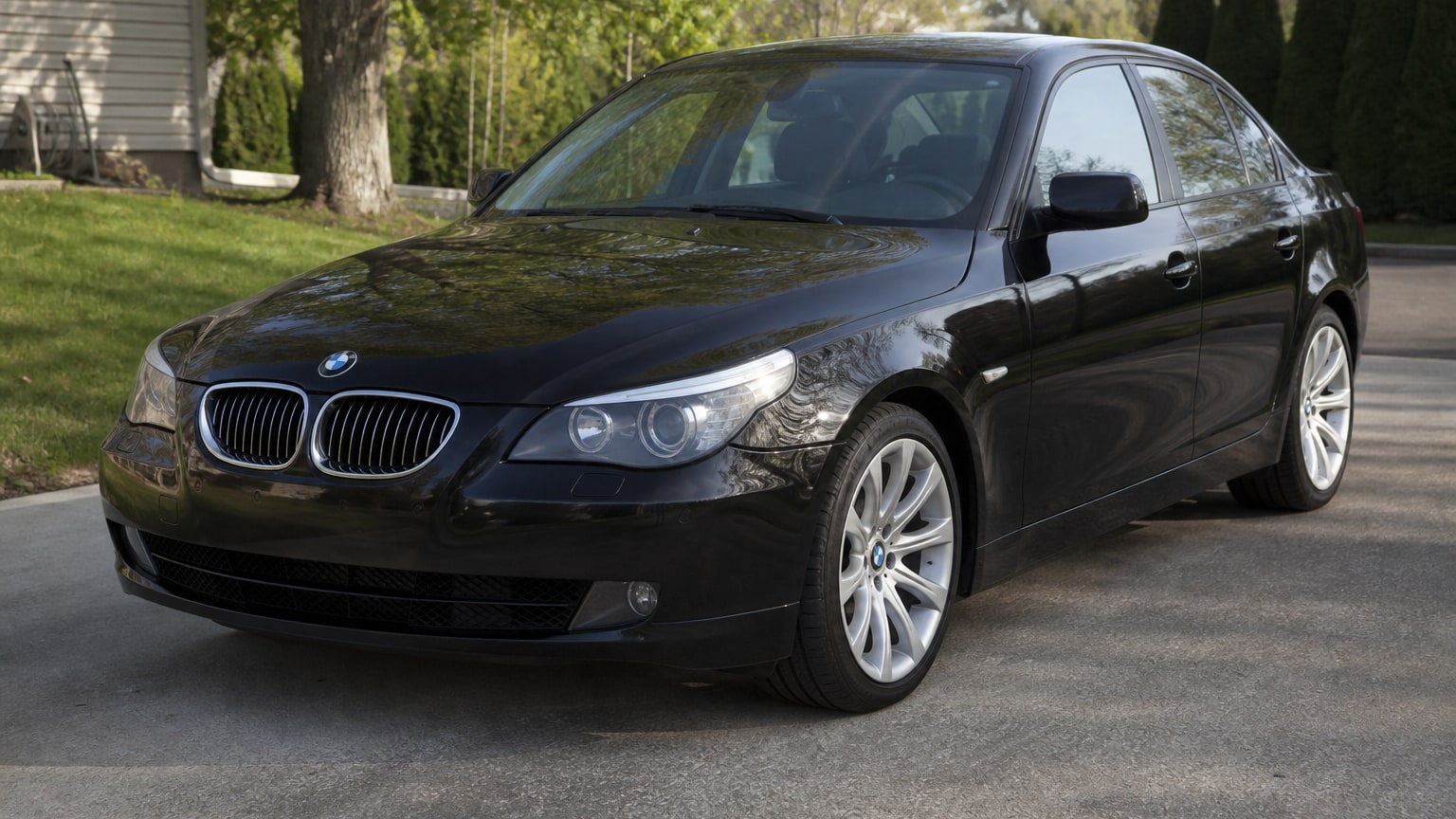 A black late-2000s BMW 5 Series sedan parked in a suburban driveway.