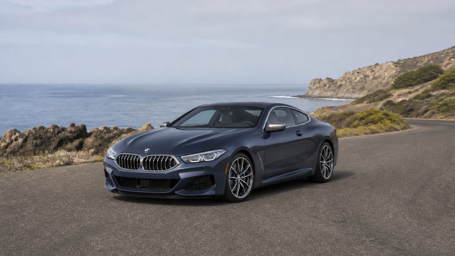A late-model 2022–2023 BMW 8 Series on a quiet coastal road.