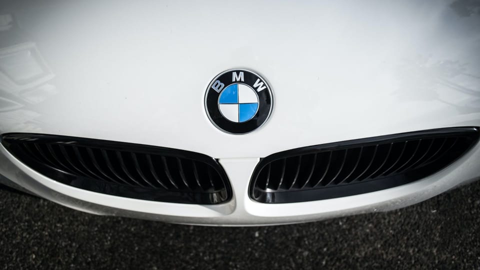 the front end of a white bmw car.|a silver car parked in front of a forest.|a close up of the tail lights of a car.
