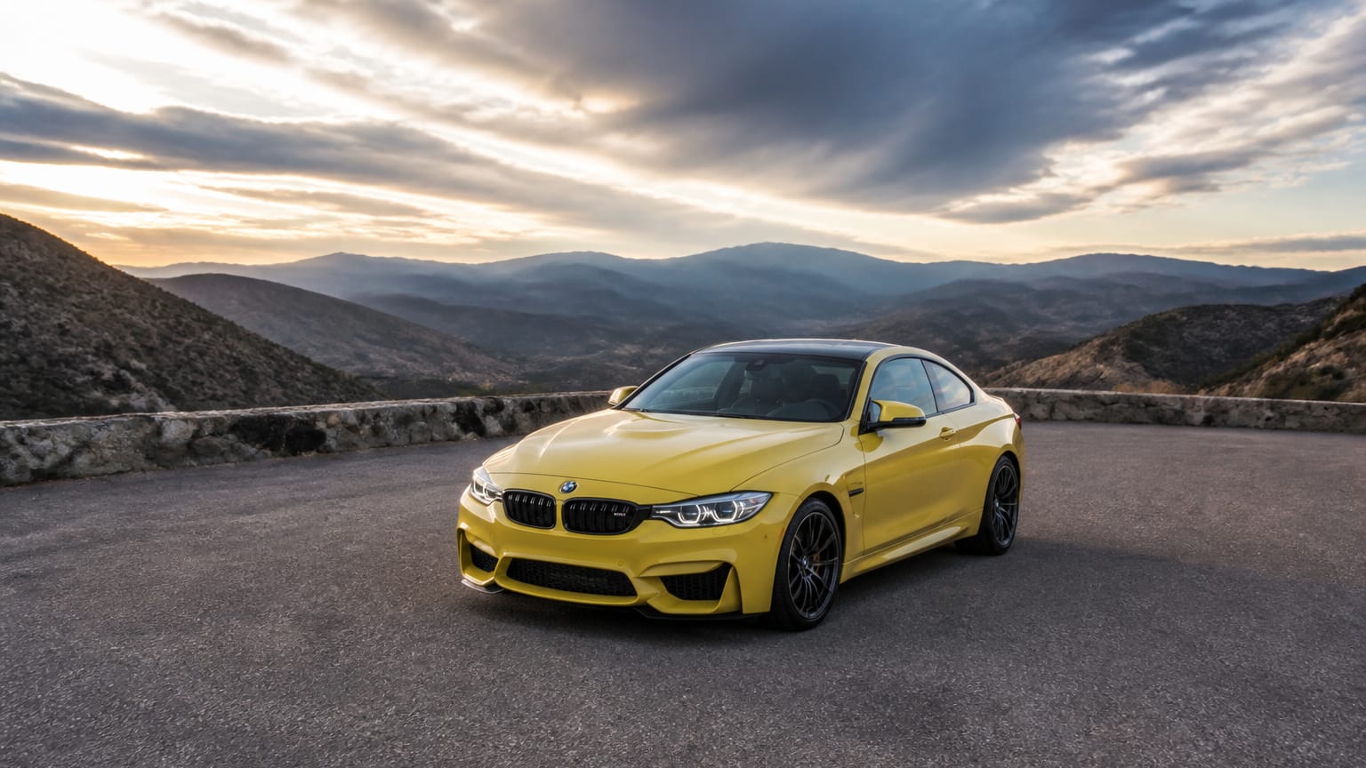 A yellow BMW M2 coupe parked on an empty mountain road overlook.