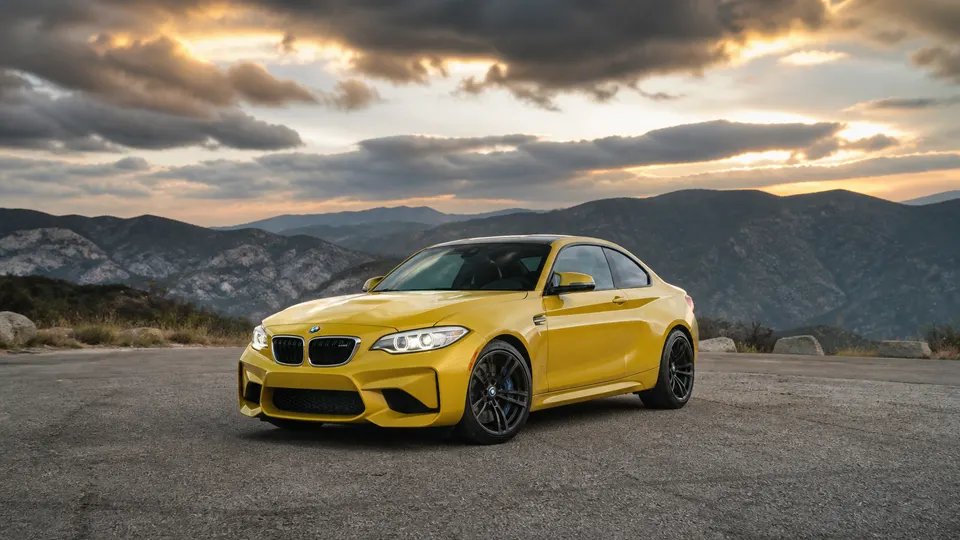 A Sao Paulo Yellow BMW M2 coupe, three-quarter front view, parked on an empty mountain road.