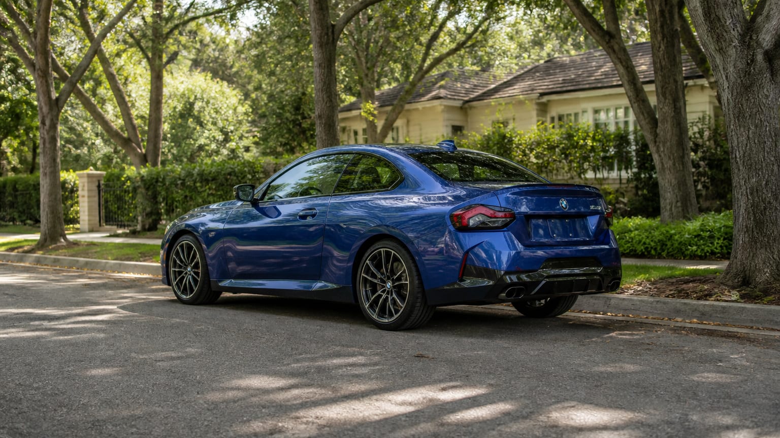 A blue BMW M240i coupe parked on a tree-lined residential street.