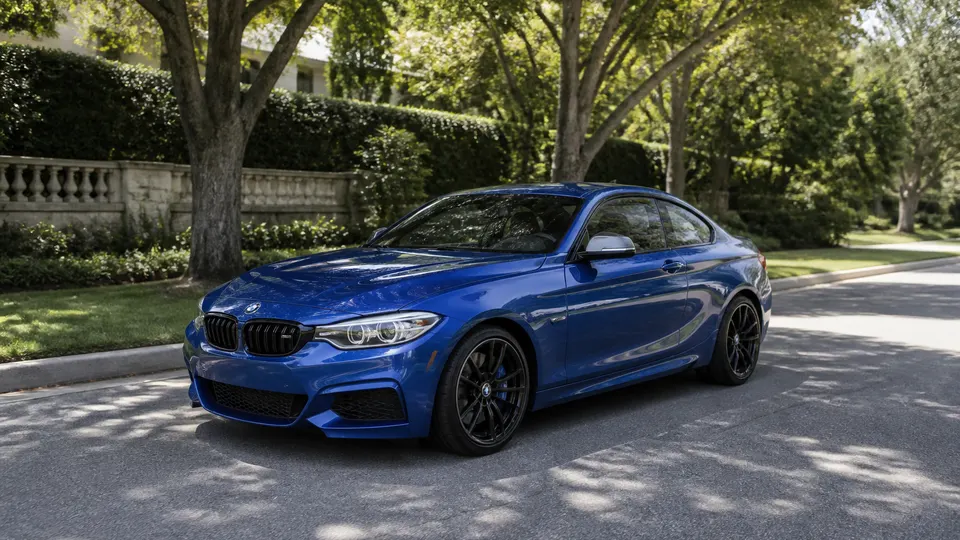 A Portimao Blue BMW M240i coupe, three-quarter front view, parked on a tree-lined residential street.
