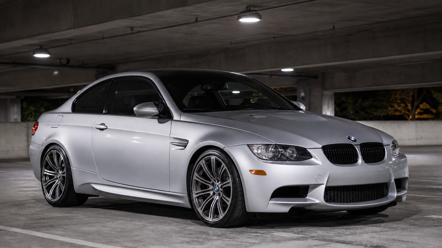 A silver E90/E92-era BMW M3 coupe in a parking garage.