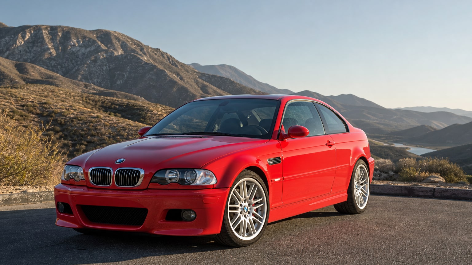 A red BMW M3 coupe parked on an empty canyon road overlook.