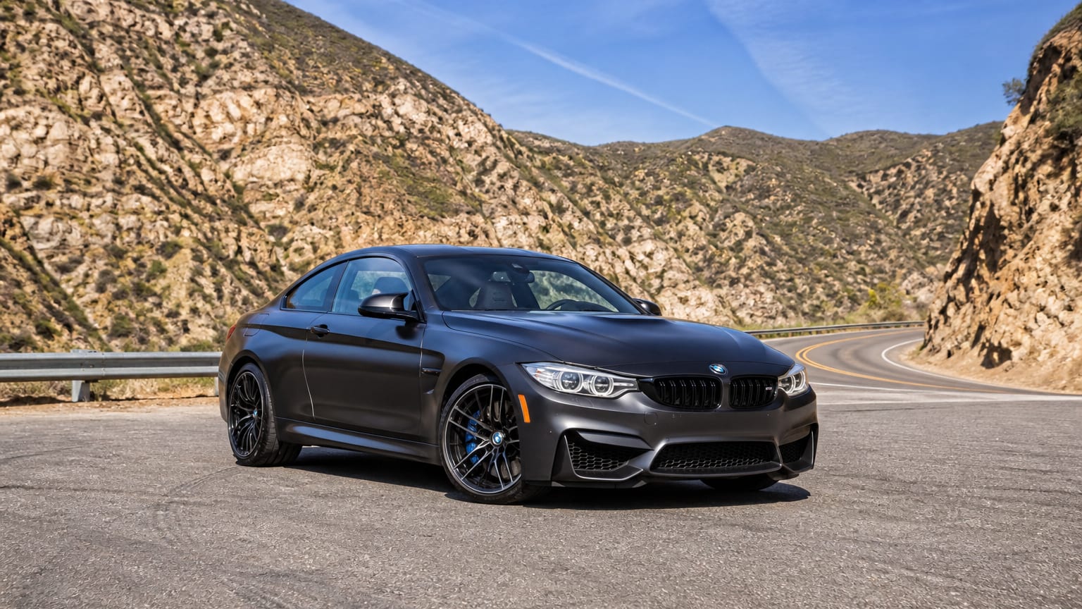 A late-model 2017 or 2022–2023 BMW M4 on a canyon road.