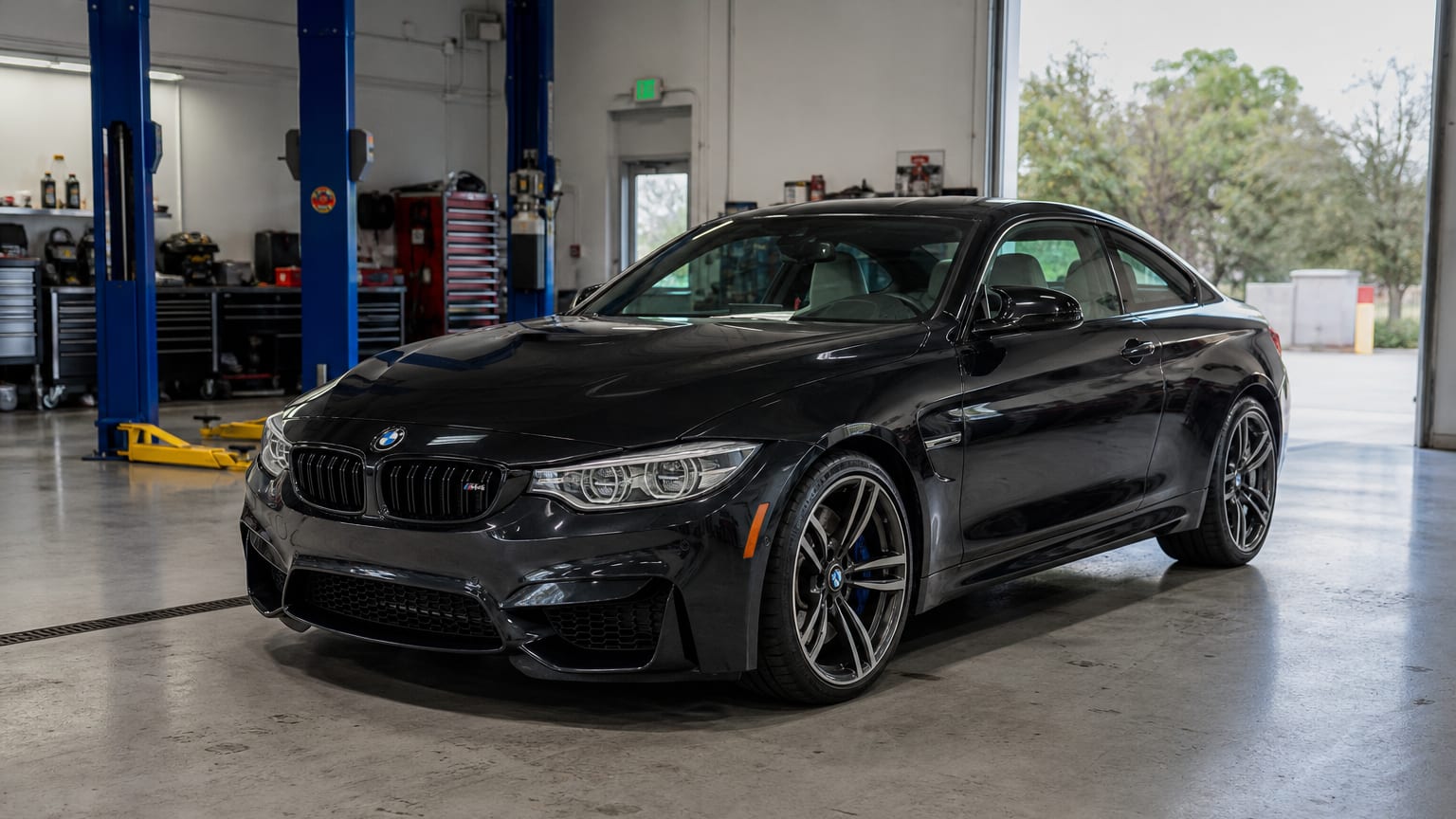 A dark 2015 or 2019 BMW M4 parked in a performance shop bay.