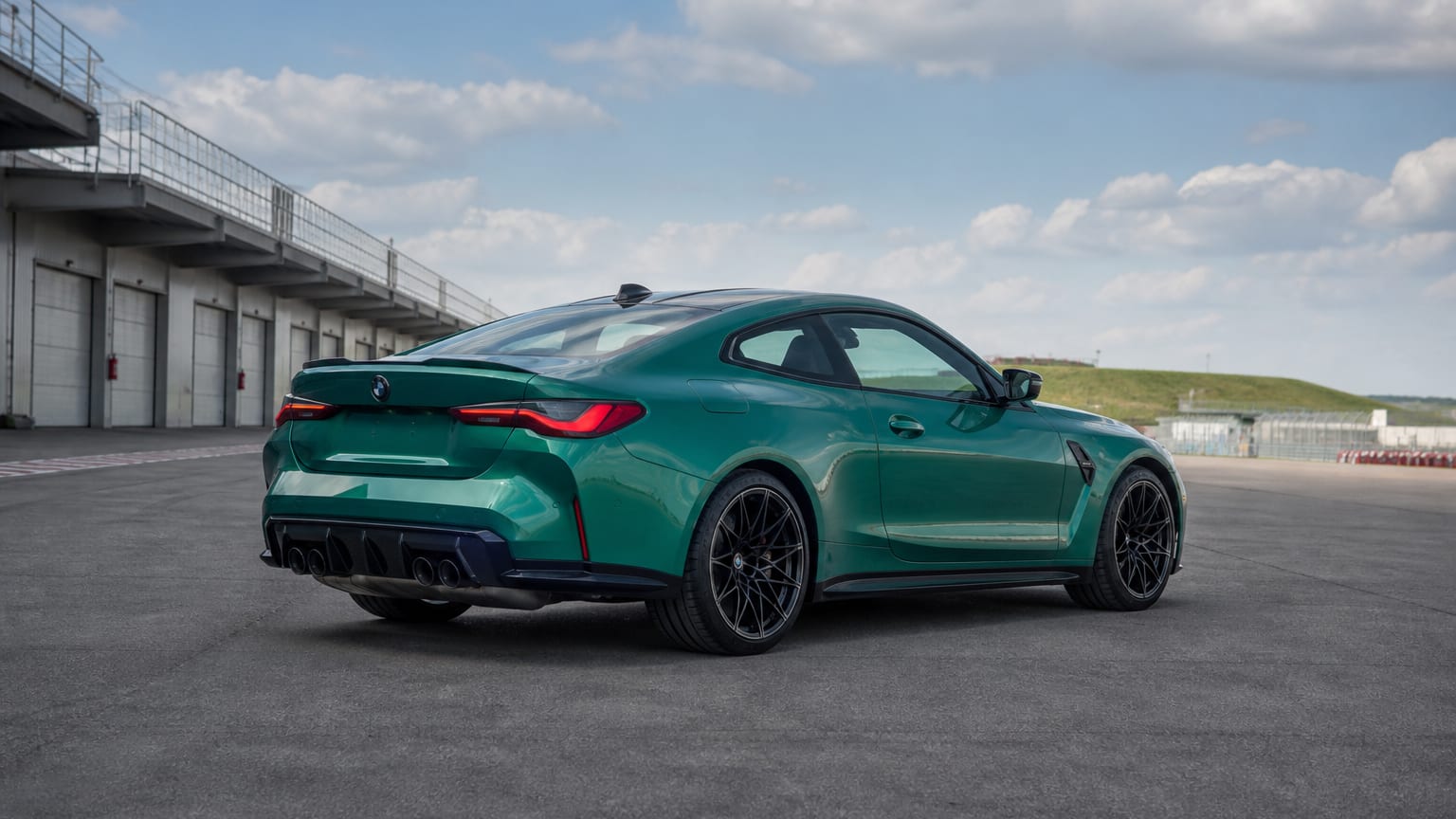 A green BMW M4 coupe parked on a racetrack paddock apron.