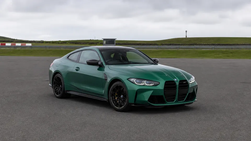 An Isle of Man Green BMW M4 coupe, three-quarter front view, parked on a racetrack paddock apron.