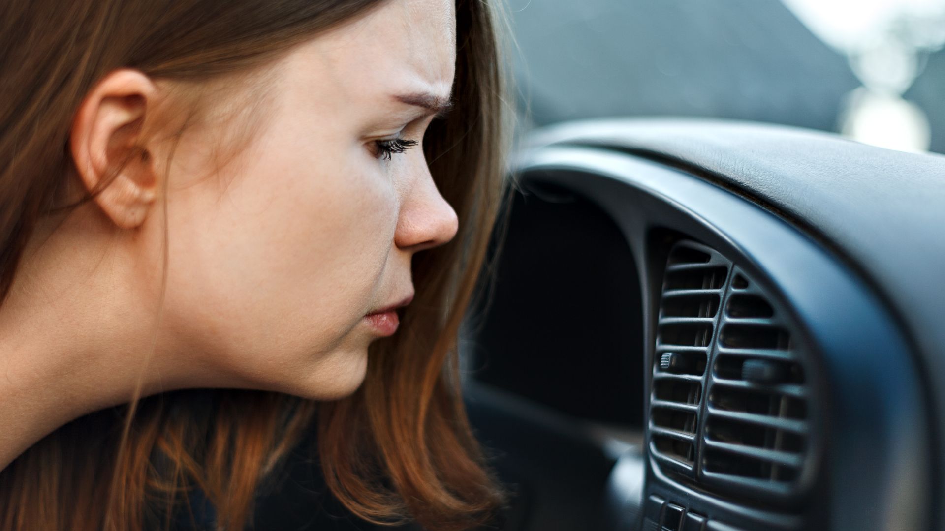 a woman looking at the air conditioner in her car.|a close up of a car's front suspension with a hole in the ground.|a person working on an engine in a car.