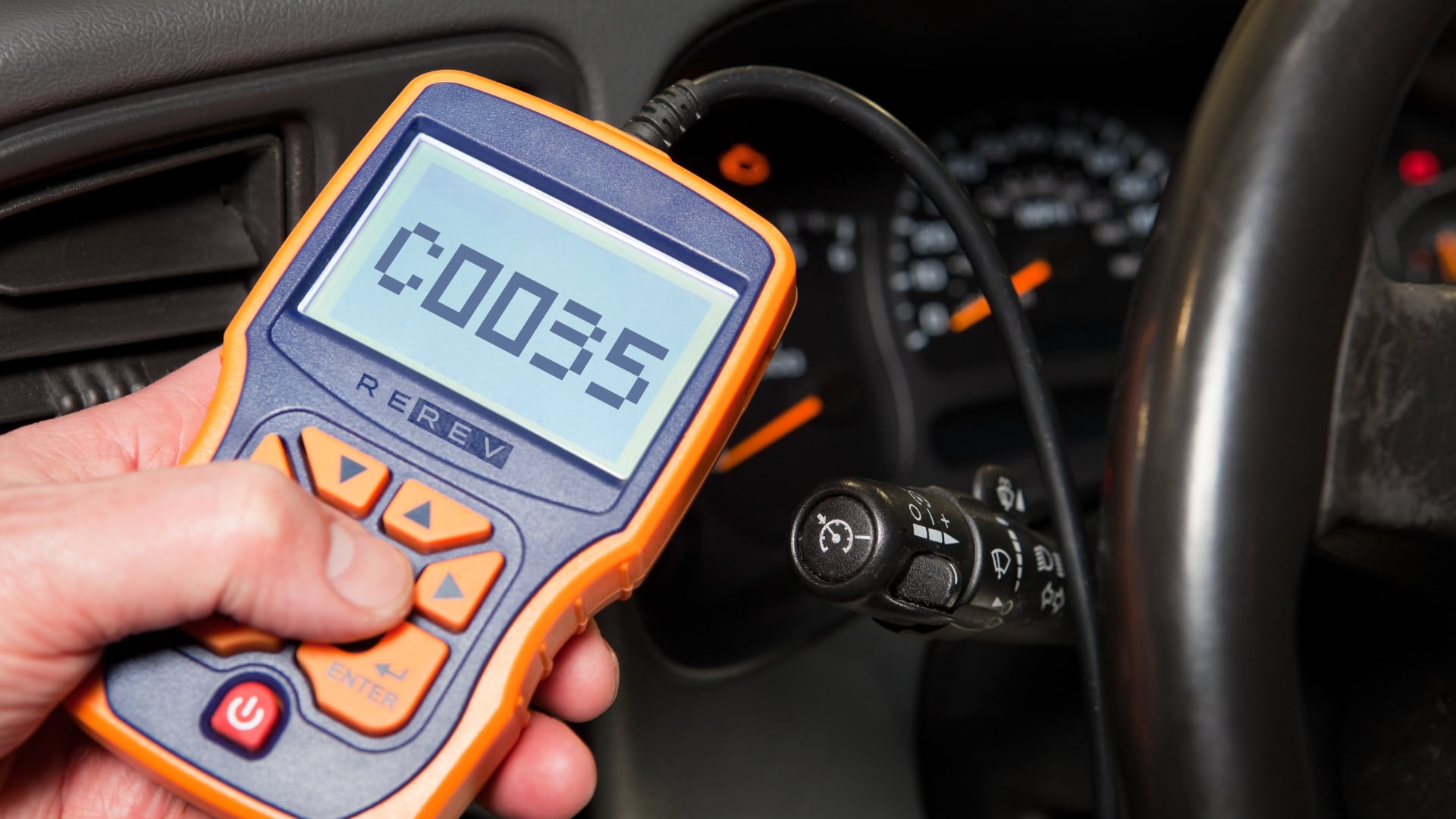 A person is holding a tire pressure gauge in a car.