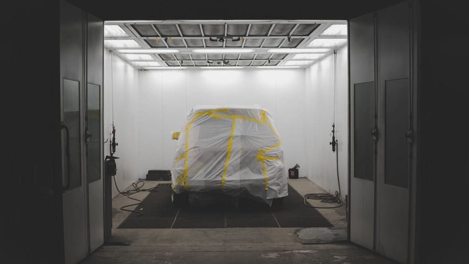 a car covered in a sheet in a garage.|a man painting a car in a garage.|a man working on a red truck in a garage.