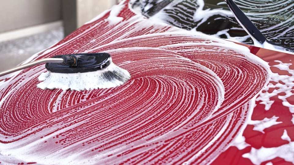 a car is covered in snow in a garage.|a man is washing his car with a hose.|a white car covered in snow on a street.|a hand in blue gloves holding a bottle of liquid.