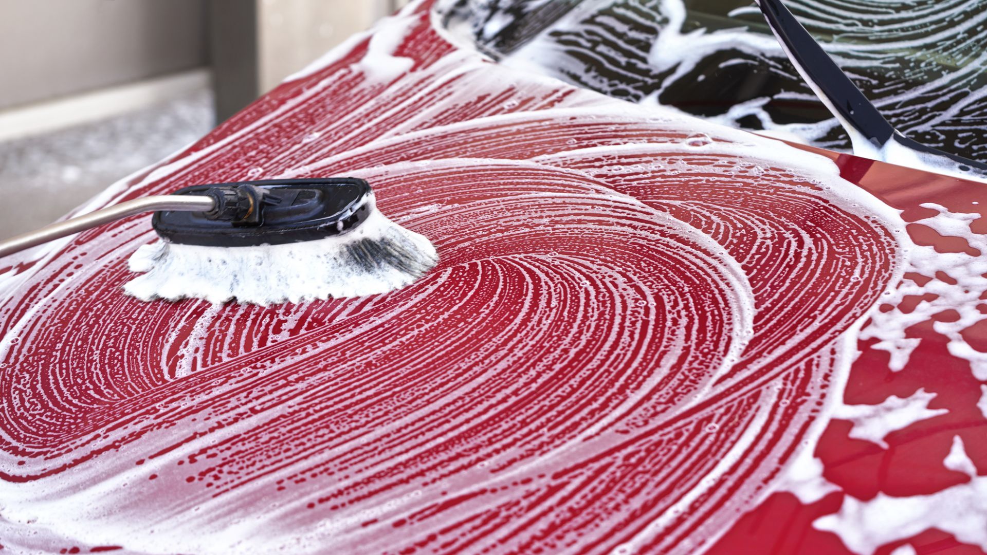 a car is covered in snow in a garage.|a man is washing his car with a hose.|a white car covered in snow on a street.|a hand in blue gloves holding a bottle of liquid.