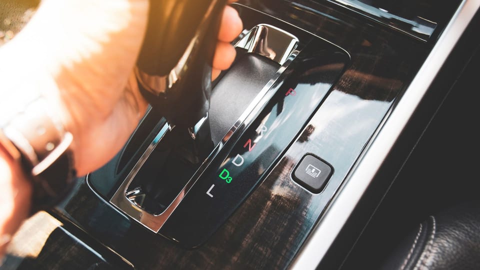 a person holding a remote control in their hand.|a close up of a gear stick in a car.|a close up of a gear stick in a car.