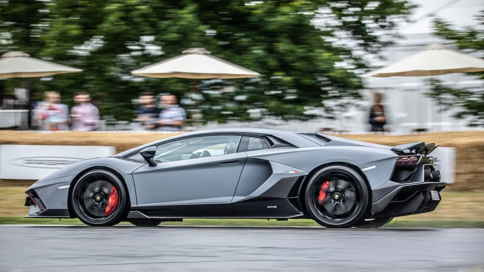 a grey sports car driving down a race track.|a yellow sports car driving on a race track.