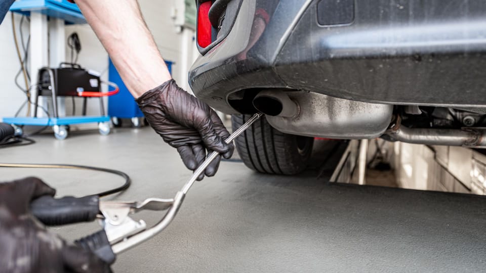 a man working on a car in a garage.|a close up of a person's hand holding a rusted pipe.