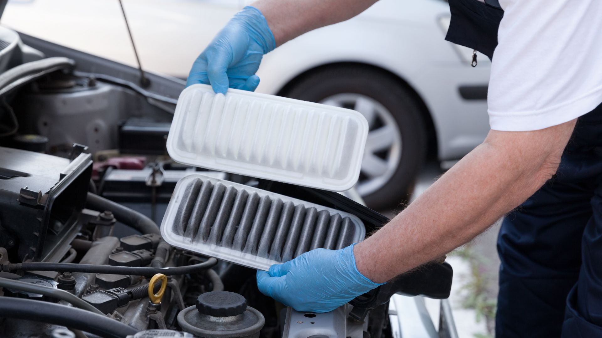 a man in a white shirt and blue gloves working on a car engine.|the engine of a red car with a filter on it.|a mechanic working on a car engine.