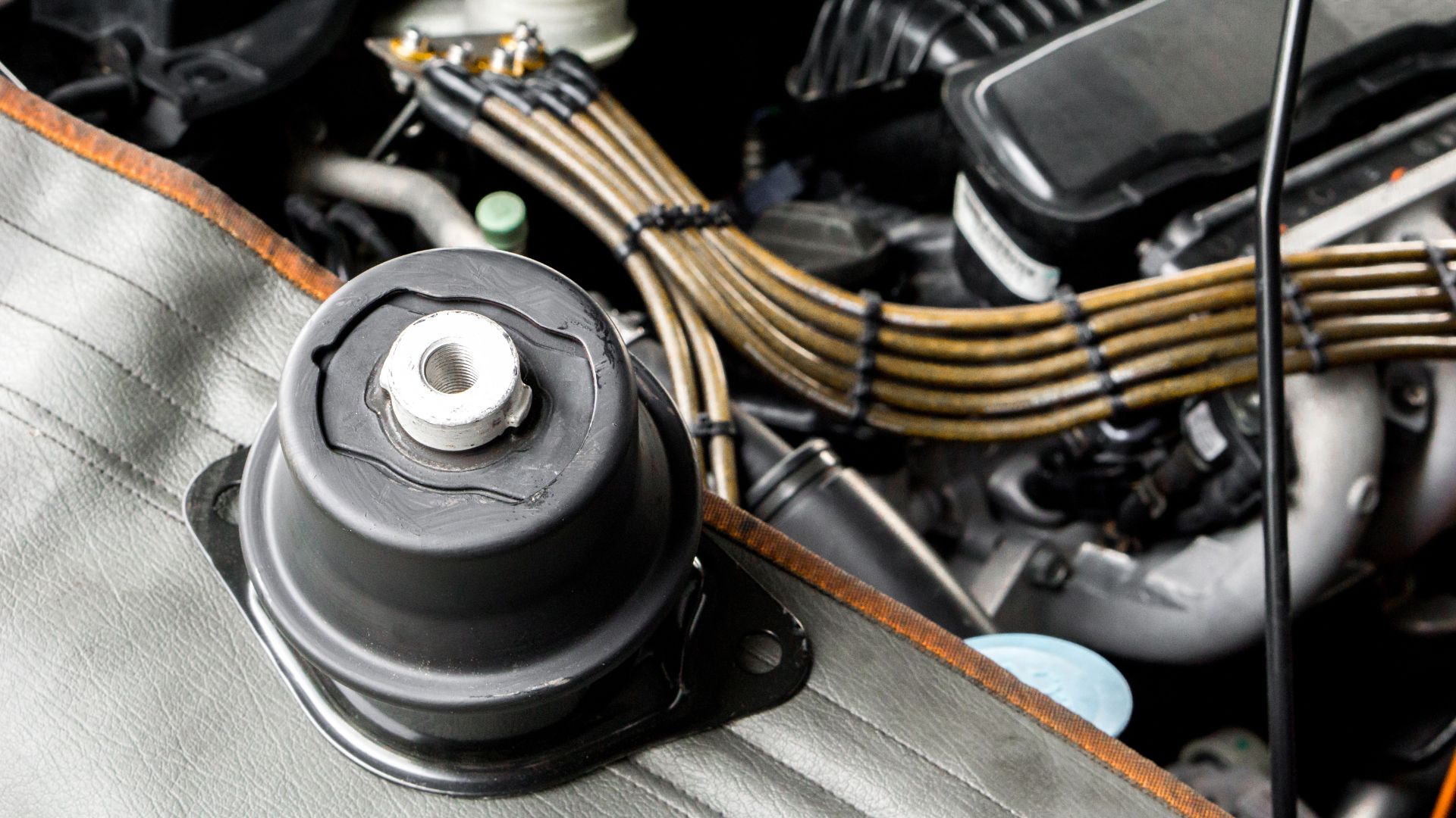 a close up of a car engine with the hood up.|a couple of pieces of metal sitting on top of a floor.|a man holding a pair of black gloves on his hands.