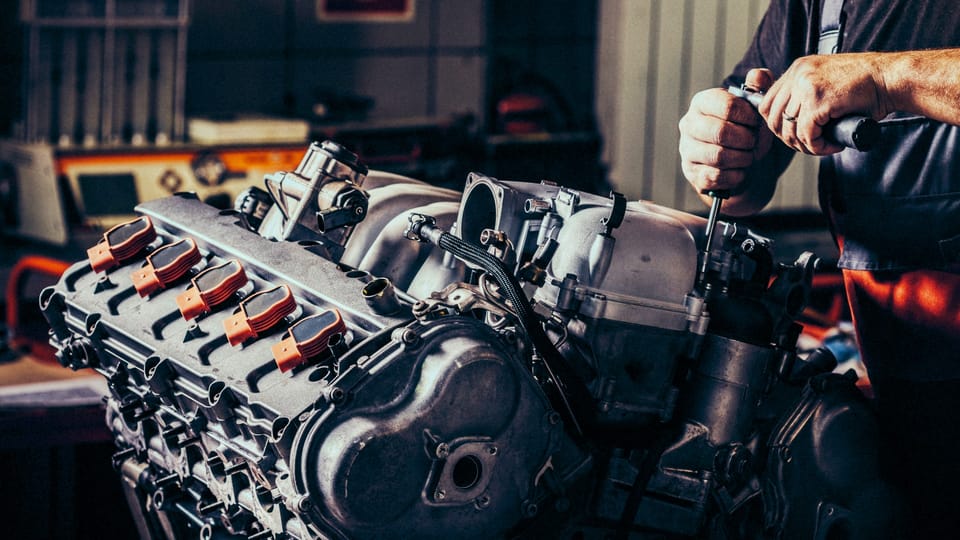A man is working on a car engine in a garage.|A white car with blue numbers on the hood.