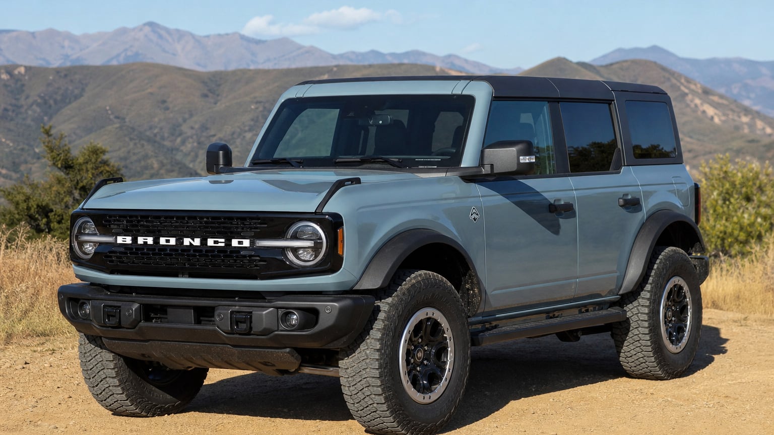 A blue sixth-generation Ford Bronco SUV parked beside a dirt trail.