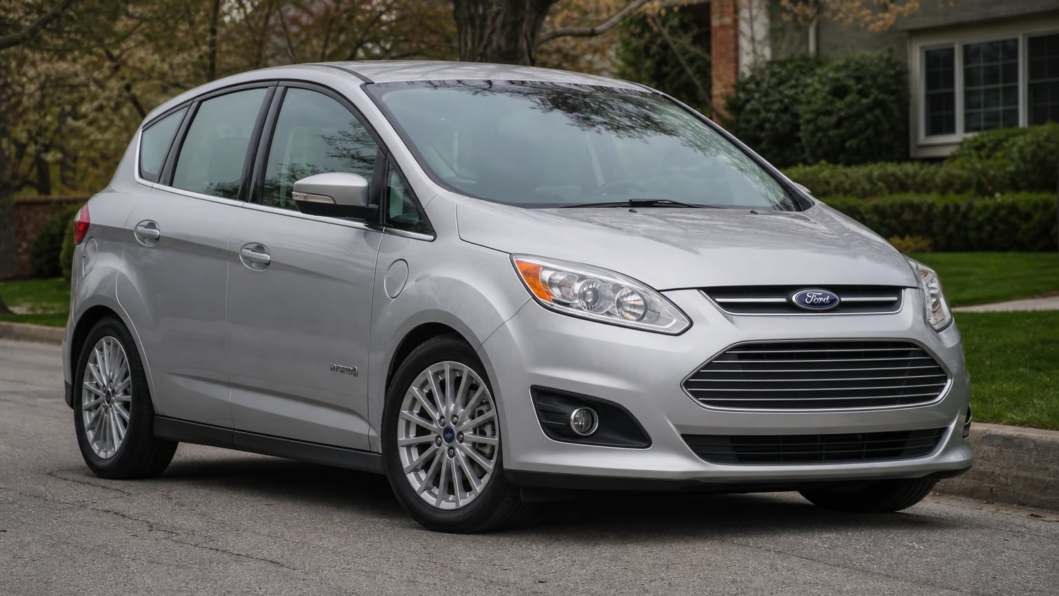 A silver mid-2010s Ford C-Max Hybrid compact hatchback parked on a suburban street.