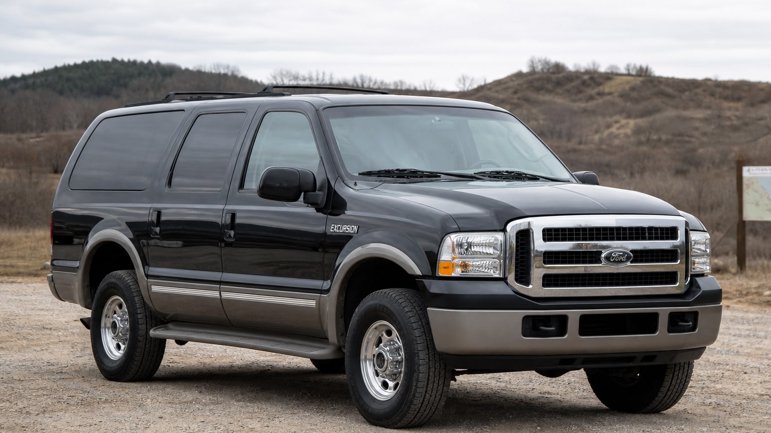A dark green mid-2000s Ford Excursion SUV parked at a trailhead.