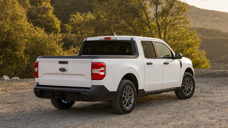 A white Ford Maverick compact pickup truck, rear three-quarter view, parked at a trailhead lot.