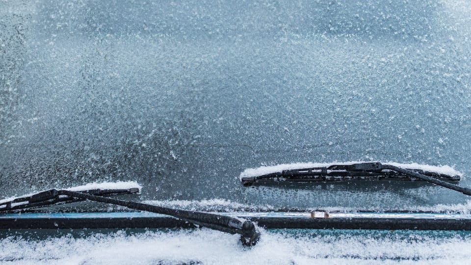 a couple of cars covered in snow next to each other.|a car covered in snow with trees in the background.|a person holding a bottle of water in their hand.|a person is cleaning a car with a brush.