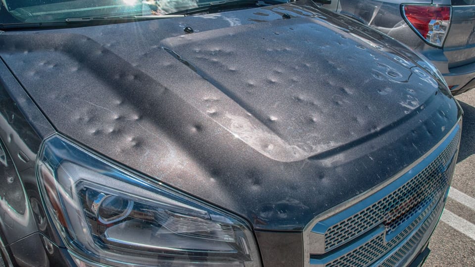a close up of a car with a mattress on the hood.|a car covered in snow with a person sitting on top of it.