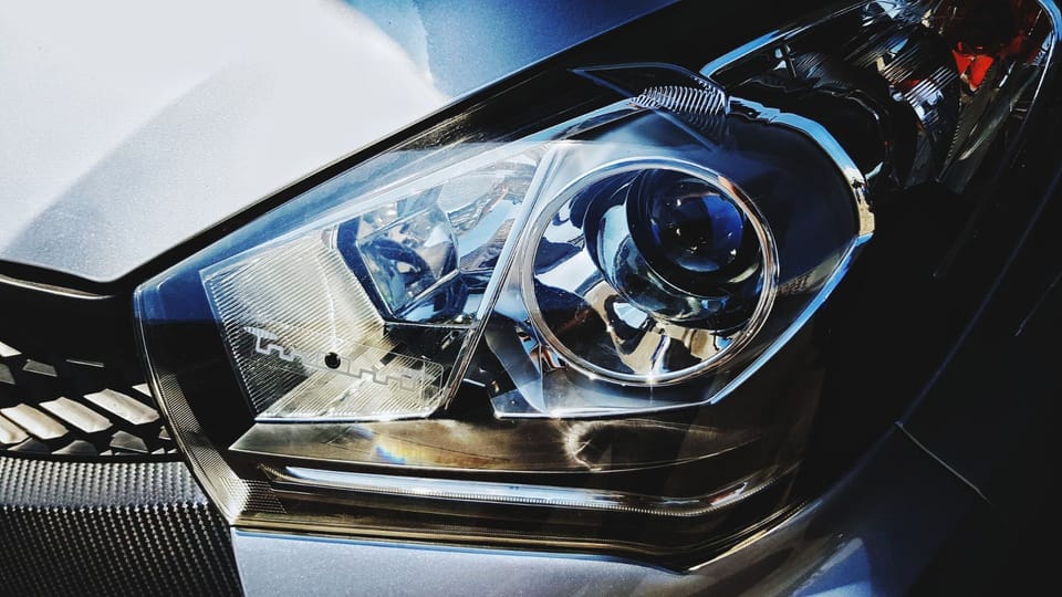 a close up of a headlight on a car.|a close up of a blue button on a car dashboard.|a close up of a person holding a camera.