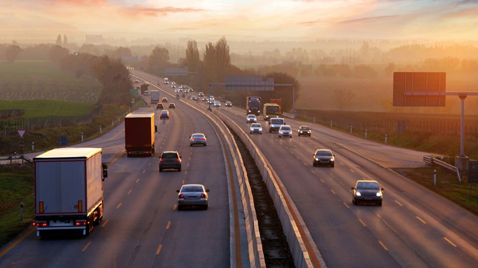 a highway filled with lots of traffic at sunset.|a white van driving down a road at night.