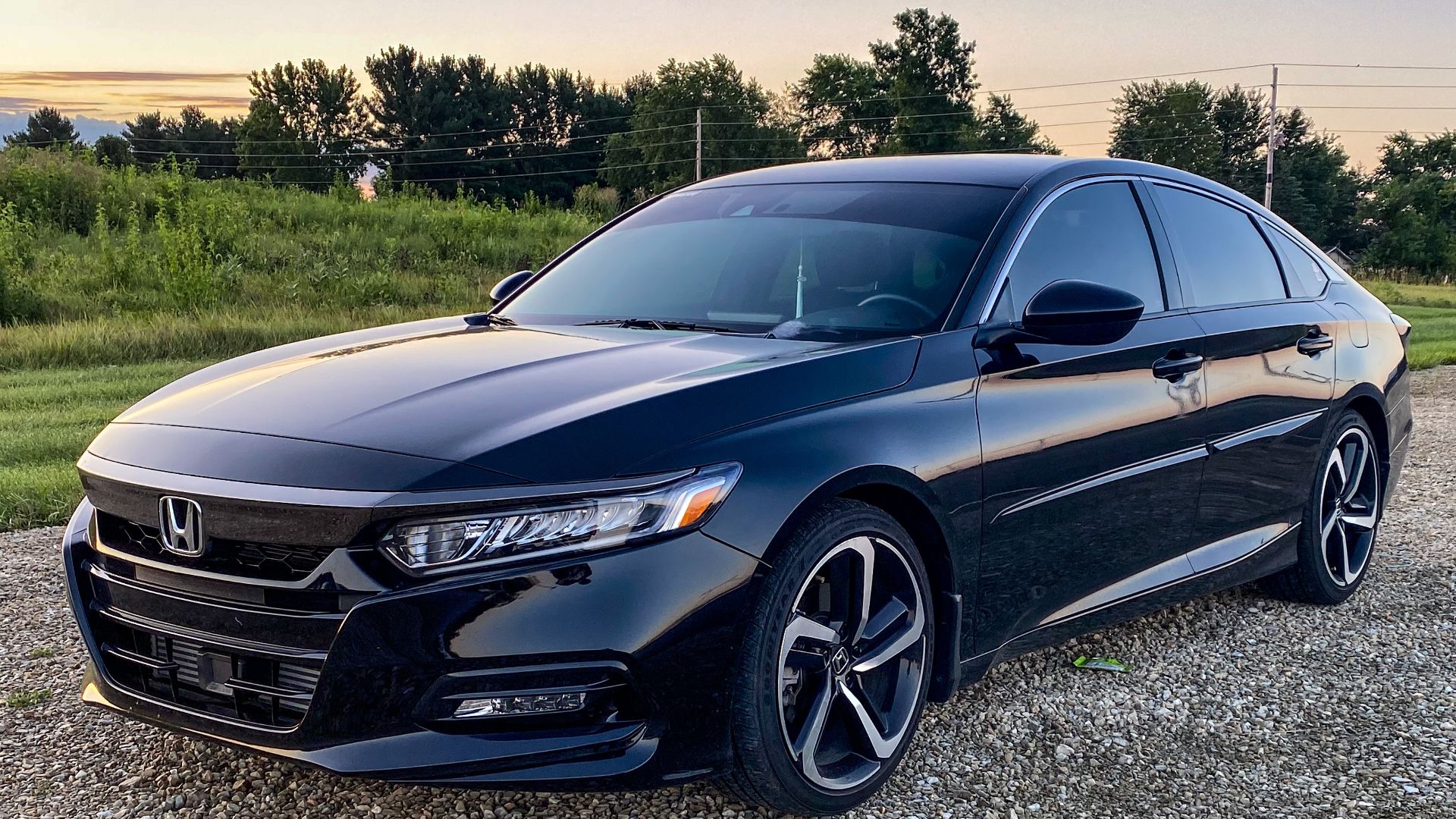 a car parked in a parking lot next to a building.|a black car parked on a gravel road.