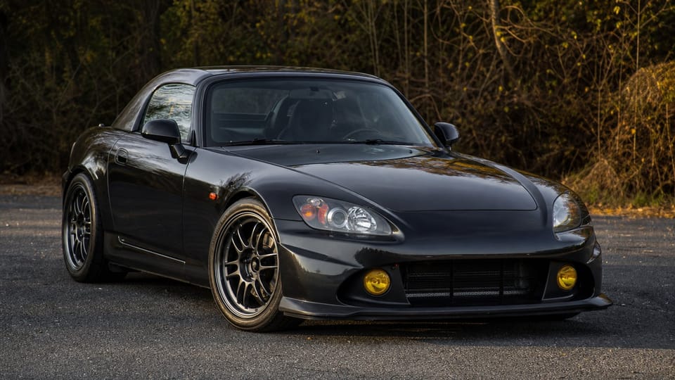 A black late Honda S2000 AP2 CR Club Racer roadster parked on asphalt.