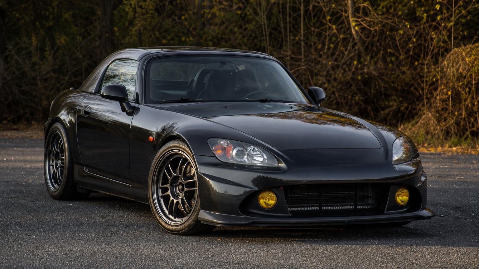 A black late Honda S2000 AP2 CR Club Racer roadster parked on asphalt.