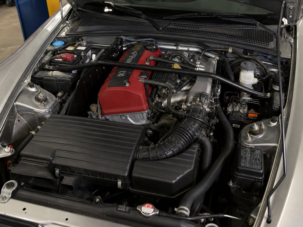 Close-up of a Honda S2000 engine bay with a red valve cover under the open hood.