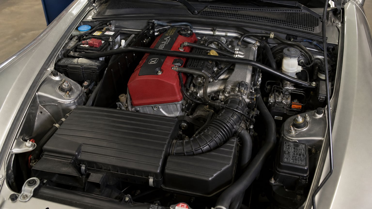 Close-up of a Honda S2000 engine bay with a red valve cover under the open hood.