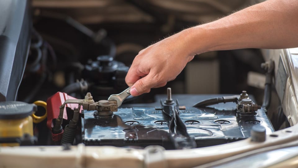 a man is working on a car's engine.|a man is working on a car battery.